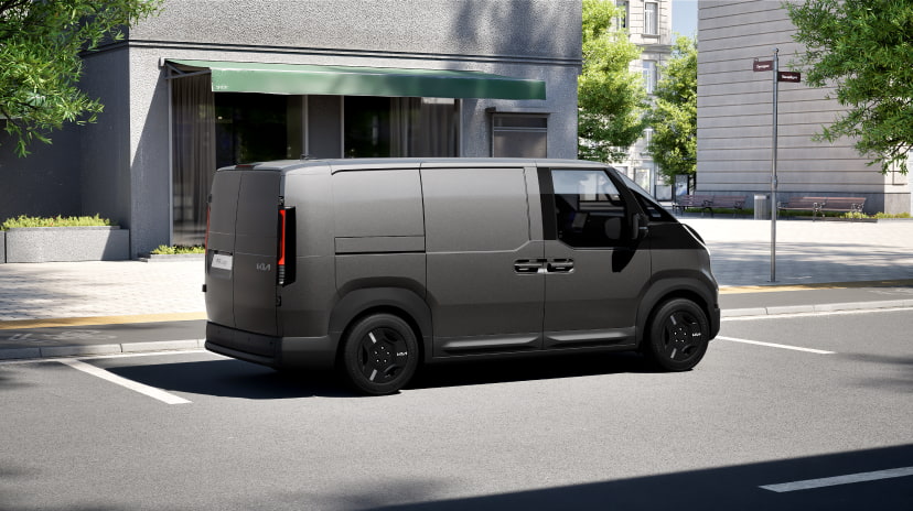 Side view of the Kia PV5 Cargo driving in an urban setting, showcasing its streamlined body and practical form
